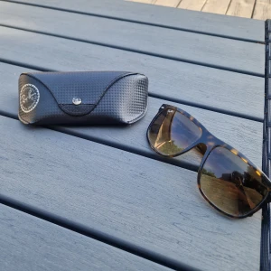 Ray-Ban solglasögon brunmelerad - Snygga Ray-Ban RB4147 solglasögon med brunmelerad båge i klassisk wayfarer-stil. Glasen är bruna och bågen har ett coolt sköldpaddsmönster. Perfekt accessoar för att lyfta din stil under soliga dagar.