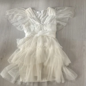 Vit volangklänning från Showpo - Superfin vit kortklänning från Showpo med flera lager volanger i tyll, v-ringning och breda transparenta ärmar. Klänningen är använd en gång och är i storlek 36