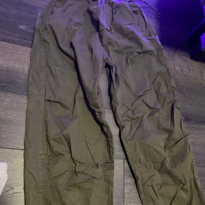 Olivgröna cargopants med snörning - Säljer ett par olivgröna cargopants med dragsko i midjan och stora sidofickor. Byxorna har en loose fit och är tillverkade i bomull, perfekta för en chill och avslappnad stil. Aldrig använda. Beställda på zelando 