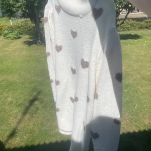 Vit stickad tröja med hjärtan - Supergullig vit stickad tröja med bruna hjärtan över hela. Tröjan har rund halsringning och långa ärmar. Perfekt för dig som vill ha en mysig och söt look med lite extra kärlek i outfiten. Andvänd en gång stor i storlek .ni betalar frakt så 