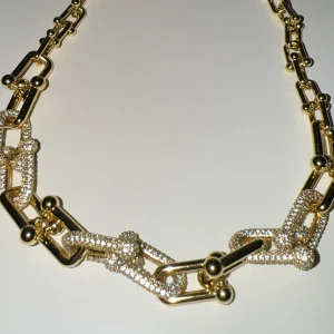 Chunky guldhalsband med glittriga länkar - Snyggt chunky halsband i guld med stora, rektangulära länkar och små kuldetaljer. Några av länkarna är täckta av glittrande stenar som ger extra bling. Perfekt statement piece för att lyfta vilken outfit som helst.