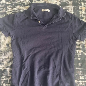 Mörkblå pikétröja från Zara - Säljer en stilren mörkblå pikétröja från Zara i storlek 164. Tröjan har klassisk krage, korta ärmar och två knappar vid halsen. Perfekt för dig som gillar en enkel och clean look. Materialet är mjukt och skönt, troligtvis bomull.
