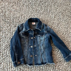 Jeansjacka från Wonder Nation - Snygg blå jeansjacka från Wonder Nation med slitna detaljer och fransad nederkant. Klassisk modell med knappar framtill, bröstfickor och lång ärm. Perfekt för dig som vill ha en cool och avslappnad stil. Storlek: 4år