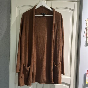 Brun kofta från H&M Basic, storlek M - Mysig brun kofta från H&M Basic i storlek M. Koftan är stickad, har lång ärm och två stora fickor framtill. Den är öppen framtill utan knappar eller dragkedja och har en avslappnad passform som passar perfekt till lager-på-lager-stil.