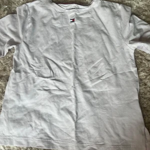 Vit t-shirt från Tommy Hilfiger - Vit t-shirt från Tommy Hilfiger med klassisk rund hals och broderad logga på bröstet. Tillverkad i mjuk bomull och har en enkel, clean design som passar till allt. Perfekt för dig som gillar stilrena och tidlösa plagg. Köpt på sellpy men jag har aldrig använt den men den är väldigt använd🤍