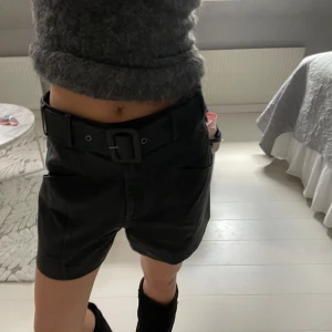 Svarta skinshorts med bälte - Snygga svarta shorts med hög midja och brett bälte i midjan. Från twist and tango