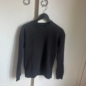 Svart basic sweatshirt - En stilren svart sweatshirt med rund hals och långa ärmar. Tröjan har en klassisk passform och ribbade muddar vid ärmslut och nederkant. Perfekt att matcha med jeans eller joggers för en enkel och clean look.