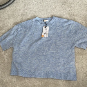 Ljusblå stickad tröja Gina Tricot - Supersöt ljusblå stickad tröja från Gina Tricot med kort ärm och ribbade detaljer vid hals, ärmslut och nederkant. Perfekt för dig som gillar en chill och enkel stil. Mjuk och skön, passar till både jeans och kjol. Tröjan är ganska kort för storleken så ni vet! 