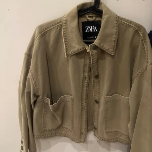 Grön jacka från Zara - Säljer en grön helt oanvänd jacka från Zara med en klassisk krage och stora fickor framtill. Jackan har långa ärmar och en avslappnad passform. Perfekt för en stilren look.