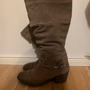 Bruna mockastövlar med nitar - Snygga bruna stövlar i mocka med dekorativa nitar och en bekväm klack. De har en dragkedja på sidan för enkel på- och avtagning. Perfekta för en stilren look.