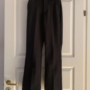 Svarta kostymbyxor från BikBok - Snygga svarta kostymbyxor från BikBok med en klassisk design. Byxorna har en flared passform. De har en dragkedja och knapp framtill för enkel stängning. Perfekta för en stilren look.