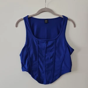 Blå korsettopp från Shein - Snygg blå korsettopp från Shein med breda axelband och en stilren design. Perfekt för att ge en trendig touch till din outfit. Tillverkad i ett glansigt material som ger en lyxig känsla.