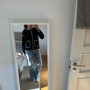 Svart kofta med vita detaljer - Säljer en stilren svart kofta med vita kantdetaljer och knappar framtill. Koftan har två framfickor och långa ärmar. Perfekt för en elegant och avslappnad look.