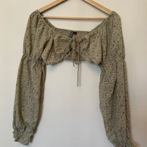 Blommig blus från Pieces - Säljer en söt blommig blus från Pieces. Den har långa ärmar med resår vid ärmslut och en knytning framtill. Perfekt för en somrig look!