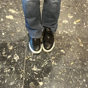 Svarta sneakers från Alexander McQueen - Snygga svarta sneakers från Alexander McQueen med vit sula och klassisk snörning. Perfekta för en stilren look med en touch av lyx. Skorna har en rund tå och är tillverkade i skinn.