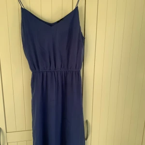 Blå klänning från Vero Moda - Säljer en stilren blå klänning från Vero Moda med smala axelband och v-ringning. Klänningen har en elastisk midja för en bekväm passform. Syns dåligt på bilden men klänningen slutar i knähöjd🫶💗