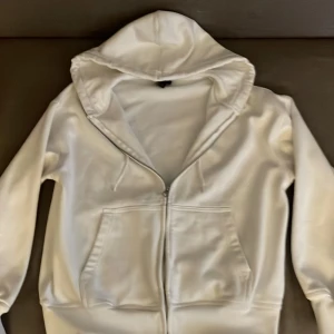 Vit hoodie från H&M - Säljer en stilren vit hoodie från H&M i oversized passform. Den har en praktisk dragkedja framtill och en stor huva. Perfekt för en avslappnad look. 🕶️