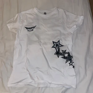 Vit t-shirt med stjärnor och åtta-motiv - Cool vit t-shirt med tryck av svarta stjärnor på framsidan och en stor åtta-boll på baksidan. Perfekt för en avslappnad stil med en twist. Passar bra till jeans eller shorts för en casual look.