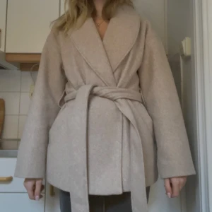Beige kappa - Säljer en beige kappa med bälte som kan även tas bort! Säljer då jag vill ha en kappa i en annan färg, den är fri från fel! Perfekt för hösten och våren, den är inte super tunn så man håller sig varm i den vilket är ett pluss. 🥰Kappan har en klassisk design med en knapp framtill. Den är lagom lång (går ner till rumpan).
