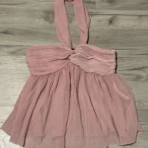 Rosa halterneck topp - Säljer en söt rosa halterneck topp med knytning i nacken. Toppen har en volangliknande design och är tillverkad i ett lätt och luftigt material. Perfekt för sommarens varma dagar, inga defekter!💞