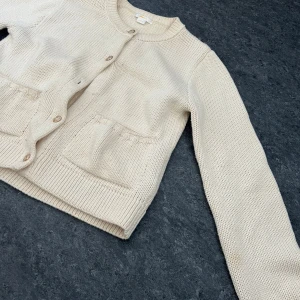 Beige stickad kofta från Gina Tricot - Säljer en mysig beige stickad kofta från Gina Tricot. Koftan har långa ärmar och knappar framtill. Perfekt för kyliga dagar och ger en stilren look. Två praktiska fickor framtill för extra förvaring. Den har tappat en knapp och har någon fläck på armen