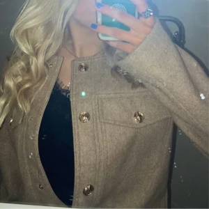 Beige kappa med knappar - Snygg beige kappa med stora knappar framtill. Jackan har en klassisk design med långa ärmar och en stilren look. Perfekt för att hålla stilen i kyligare väder.