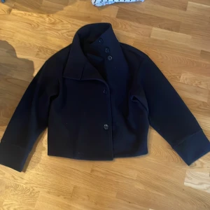 Marin blå  kappa med knappar - Elegant marin blå  kappa med knappar framtill. Den har en klassisk krage och långa ärmar. Perfekt för en stilren look.