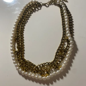 Halsband med pärlor och kedjor - Unikt halsband med en kombination av vita pärlor och guldiga kedjor. Kedjorna har små spetsiga detaljer som ger en edgy look. Perfekt för att lyfta vilken outfit som helst.