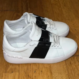 Valentino Garavani sneakers - Snygga vita Valentino Garavani sneakers med svart detalj över snörningen. Skorna är helt nya. Låda och kvitto kommer med vid köp.