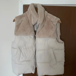 Beige pälsväst med dragkedja - Säljer en mysig beige pälsväst med dragkedja. Aldrig använd, jättefin och skön. 