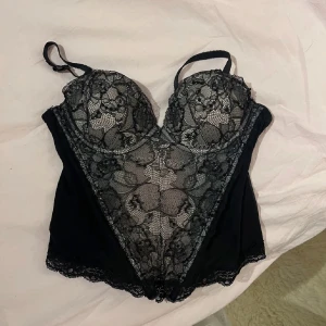 Svart spetskorsett - Elegant svart korsett med vacker spetsdetalj och justerbara axelband. Meshen har litet hål på men bara det yttersta lagret. Syns inte när man har på den