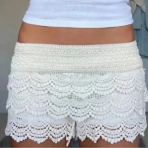 Vita spets shorts - Snygga vita shorts med spetsdetaljer och volangdesign. Perfekta för en somrig look. De har en elastisk midja för extra komfort.