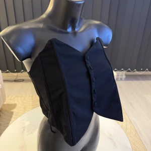 Svart korsettliknande topp - Snygg svart korsettliknande topp med knappar framtill. Perfekt för en stilren look. Passar bra till både jeans och kjol. Passar parfekr i M/L storlek.