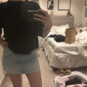 Ljusblå jeanskjol -  ljusblå jeanskjol med en klassisk femficksdesign. Kjolen är kort och har en rå kant nertill för en trendig look. Perfekt för sommardagar! Kjolen är klippt av oss för att den ska vara en ”minikjol”. Modellen på bilden brukar ha storlek 36/38 och kjolen sitter perfekt. 