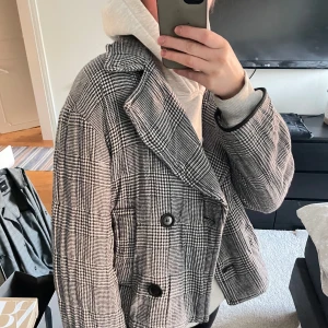 Rutig kavaj från Zara - Snygg rutig kavaj från Zara i svart och vit. Kavajen har en klassisk dubbelknäppt design med stora knappar och långa ärmar. Perfekt för en stilren look.