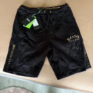 Svarta shorts från BOSS med gulddetaljer - Hugo boss kortbyxor helt nya vanliga ej badbyxor storlek S men är som M 700 kr ny pris 1200kr Har du inte råd skriv inte.  inget sist kompis pris.
