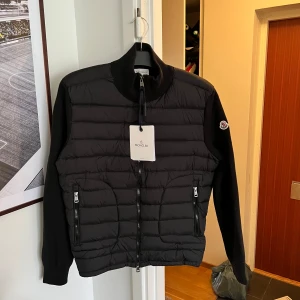 Svart pufferjacka från Moncler - Säljer en svart pufferjacka från Moncler med quiltad front och ärmar i mjukare material. Jackan har dragkedja framtill och två dragkedjeförsedda fickor. Klassisk Moncler-logga på ärmen och hög krage. Storlek L men passar M, säljer pga för liten.