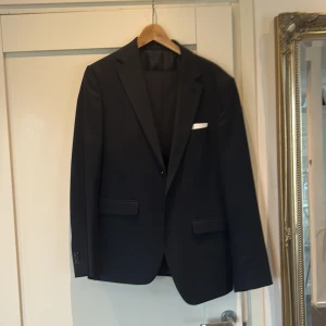 Svart kostym från Riley Slim Fit, pris kan diskuteras  - Säljer en stilren svart kostym från Riley i slim fit-modell. Kavajen har två knappar, fickor med lock och en bröstficka med vit näsduk. Byxorna är raka och matchar kavajen perfekt. Perfekt för bal eller fest.