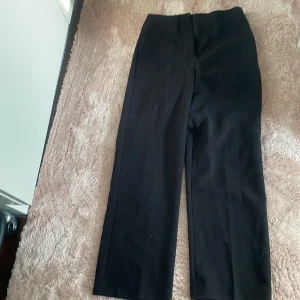 Svarta kostymbyxor från Vero Moda - Säljer ett par klassiska svarta kostymbyxor från Vero Moda i storlek XS. Byxorna har hög midja, raka ben och stängs med dragkedja och knapp i sidan. Perfekta för en stilren och enkel look.