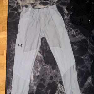 Ljusgrå vindjacka med huva från Under Armour. Samt likadan färg på byxorna. Storlek M på byxorna, och storlek S/M på jackan men den är en längre modell - Säljer en ljusgrå vindjacka från Under Armour med huva och svarta dragkedjor. Jackan har lång ärm, två fickor med dragkedja och en stilren logga på bröstet. Perfekt för träning utomhus när det blåser.Byxorna är samma färg och är då tillsammans en dress. Säljer dressen för 1500 och skicket är som ny 