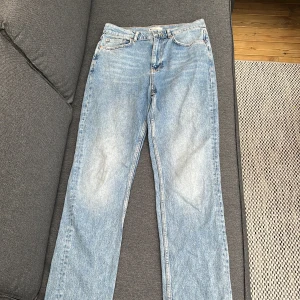 Blå raka jeans från Gina Tricot - Klassiska blå jeans från Gina Tricot med raka ben och femficksmodell. Jeansen har normal passform och är tillverkade i ett robust denimtyg. Perfekta för en avslappnad stil.