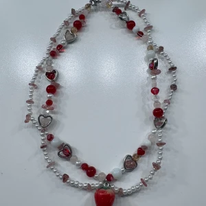 Halsband med röda pärlor och hjärtan - Dubbelradigt halsband med vita och röda pärlor, små stenar och silverfärgade hjärtan. Stort rött hjärta som hänge. Perfekt för dig som gillar färg och lekfulla detaljer.