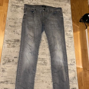 Grå slim fit jeans från Jack & Jones - Säljer ett par gråa slim fit jeans från Jack & Jones, modell SLM/GLENN. Jeansen har klassisk femficksdesign, dragkedjegylf och snyggt tvättad look. Perfekta för dig som gillar en smalare passform och stilren design. Storlek 34/32
