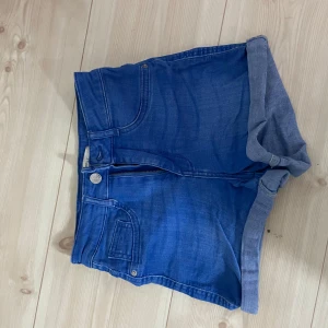 Blå jeansshorts från Gina  - Snygga blå jeansshorts från med klassisk femficksdesign och uppvikta benslut. Shorts med knapp och dragkedja framtill samt bakfickor. 