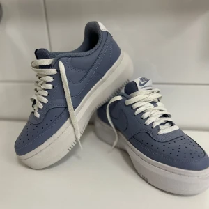 Nike Court Vision Low sneakers i blått - Snygga Nike Court Vision Low sneakers i en matt blå färg med vita detaljer och vit sula. Skorna har klassisk snörning, perforerad tå och en bekväm innersula med Nike-logga. Perfekta för dig som gillar stilrena och sportiga sneakers. Aldrig använda utomhus.