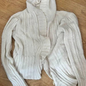 Vit stickad kofta med knappar - Säljer en mysig vit stickad kofta med bred krage och två stora knappar framtill. Koftan har lång ärm och ribbade muddar vid ärmslut och nederkant. Perfekt för lager-på-lager och chill dagar.