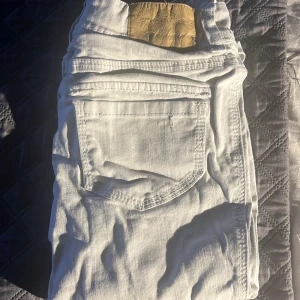 Vita jeansbyxor med raka ben - Säljer ett par vita jeansbyxor med raka ben och klassiska fickor både fram och bak. Byxorna har bälteshällor och knäppning framtill. Perfekta för en stilren och fräsch look.