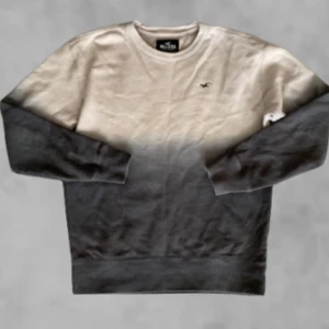 Ombre sweatshirt från Hollister - Snygg sweatshirt från Hollister med ombre-effekt i beige och svart. Tröjan har rund halsringning och långa ärmar. Perfekt för en avslappnad och trendig stil.