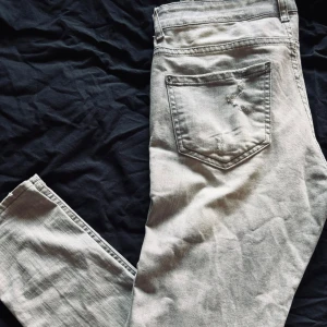 Ljusgrå jeansbyxor från Dsquared2 ICON - Säljer ett par ljusgrå Dsquared2 ICON jeans med slitningar och distressed detaljer framtill. Klassisk femficksmodell med Dsquared2-logga vid gylfen och stor ICON-patch bak. Raka ben och normal passform.