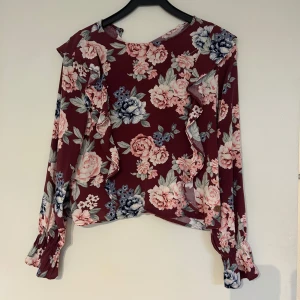Vinröd blus med blommor  - Säljer en vinröd blus med blommigt mönster i rosa, blått och vitt. Blusen har långa ärmar med volangdetaljer och en lös passform. blusen är använd några gånger men är i väldigt fin skick💕💞